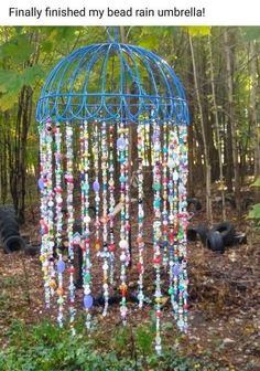 a blue birdcage with beads hanging from it's sides in the woods