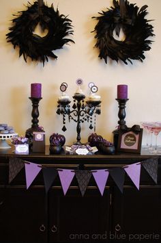 a table topped with purple and black desserts next to two wreaths on the wall