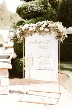 a sign with flowers on it sitting in front of a tree and shrub covered area