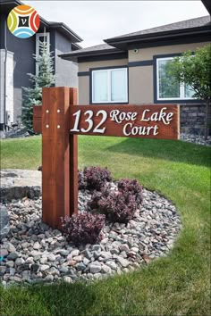 a wooden sign that says rose lake court in front of a house with landscaping around it