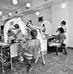 an old black and white photo of people getting their hair done in the mirror while another woman watches