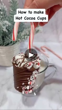 a person holding a candy cane over a hot cocoa cup filled with chocolate and marshmallows