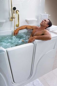 a man laying down in a bathtub filled with blue water and foam next to a toilet