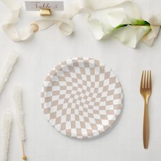 a white plate with a checkered design on it next to gold utensils