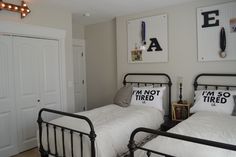 two twin beds with white sheets and black metal frames in a small room, one has an i am not tired sign on the wall