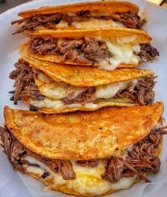 a white plate topped with three tacos covered in meat and cheese on top of tortillas