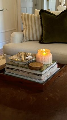 a coffee table topped with books and a lit candle on top of each other next to a couch