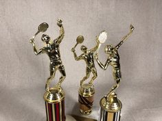 two trophies with tennis players on them and one holding a racket in the air