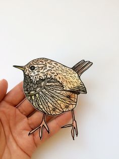 a hand holding a small bird brooch in it's right hand on a white surface