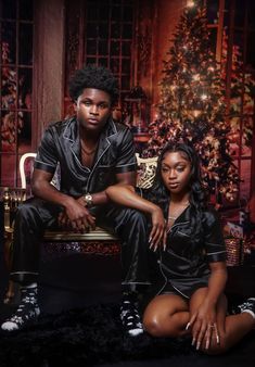 a man and woman sitting next to each other in front of a christmas tree with lights