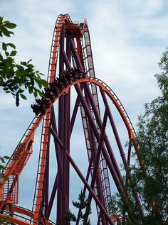 an amusement park ride with people on it's side and trees in the foreground