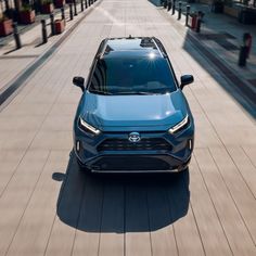 the front end of a blue toyota suv driving down a city street with buildings in the background