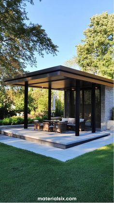 Modern outdoor patio with a flat roof, surrounded by trees and grass, featuring seating and a table. Decks And Patios