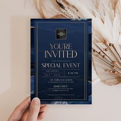 a person holding up a blue and gold party card with feathers on it, in front of a white background