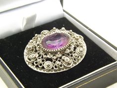 Hello and welcome to my shop. I am offering to you this very fine oval design vintage period costume jewelry brooch. As you will see in the pictures the mount is made in filigree raised work silvertone metal and set with a sparkly faceted oval purple glass stone. The clasp is a roll over pin type and is in full working order. The filigree silvertone and oval purple stone brooch is in an excellent used vintage condition with no or only very slight age related surface wear as shown. So please exam Ornate Oval Brooches For Anniversary, Ornate Oval Anniversary Brooches, Ornate Oval Filigree Brooches, Vintage Purple Oval Brooch, Silver Filigree Oval Brooches, Victorian Silver Oval Brooch, Silver Oval Filigree Brooches, Silver Oval Victorian Brooch, Purple Oval Brooch Jewelry