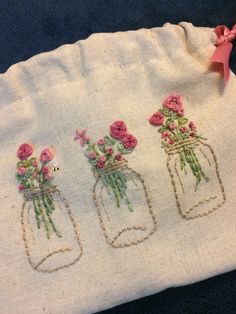 three embroidered mason jars with pink flowers on them