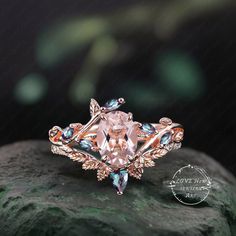 an engagement ring with pink and blue stones on top of a green mossy rock