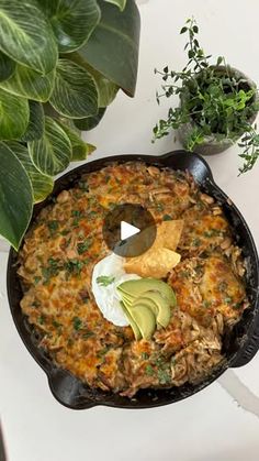 a skillet filled with food sitting on top of a table next to a potted plant