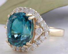 8.70 Carats Natural Very Nice Looking Blue Zircon and Diamond 14K Yellow Gold Ring Suggested Replacement Value: 9,000.00 Total Natural Cushion Shaped Zircon Weights: Approx. 7.80 Carats Zircon Measures: 11 x 8.4mm Natural Round Diamonds Weight: .90 Carats (color G-H / Clarity SI1-SI2) Ring total weight: 5.2 grams Disclaimer: all weights, measurements and colors are approximate and may vary slightly from the listed dimensions or as seen in the image. All pictures are magnified to show the smalles Blue Gia Certified Emerald Ring For Formal Occasions, Luxury Blue Topaz Ring Gia Certified, Gia Certified Blue Topaz Diamond Ring, Gia Certified Blue Topaz Ring With Diamond, Gia Certified Blue Topaz Round Cut Ring, Gia Certified Blue Topaz Ring With Round Cut, Gia Certified Yellow Gold Topaz Ring, Formal Turquoise Jewelry With Halo Setting, Blue Emerald Ring For Formal Occasions