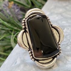 Introducing our striking Black Stone Statement Ring, a captivating piece of jewelry that combines the allure of a large, elegant black rectangular gemstone with the charm of a simple yet beautiful flower motif etched into the sterling silver ring. This statement ring features a  black gemstone and is available in a size 7.5, making it a perfect fit for those who appreciate bold and sophisticated designs. Elegant Black Gemstone: The centerpiece of this statement ring is a large rectangular black Elegant Black Jewelry With Large Stone, Black Rectangular Rings For Gifts, Rectangular Black Enamel Rings As Gift, Black Jewelry With Rectangular Stone For Gift, Rectangular Black Enamel Rings For Gifts, Black Rectangular Ring Gift, Black Rectangular Stone Jewelry For Gift, Rectangular Silver Jewelry With Black Enamel, Black Rectangular Stone Jewelry Gift