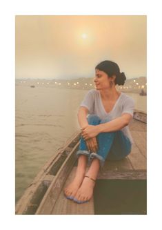 a woman sitting on top of a wooden boat in the water with her legs crossed