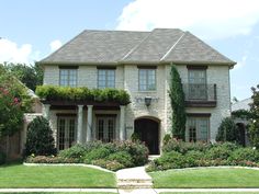 a large house with lots of plants and flowers on the front lawn, along with landscaping