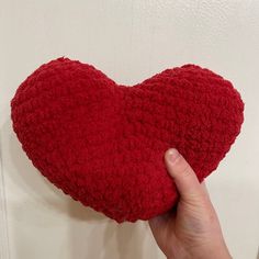 a hand holding a red heart shaped pillow