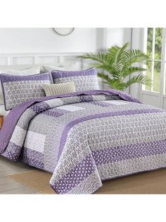 a bed with purple and white comforters in a room next to a potted plant