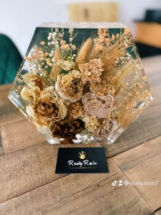 a glass vase filled with dried flowers on top of a wooden table