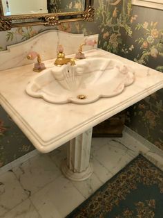 a bathroom sink sitting under a mirror in front of a floral wallpapered wall