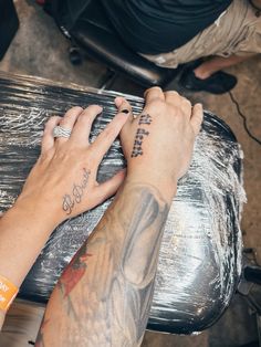 two people with tattoos on their arms are touching each other's fingers while sitting at a table