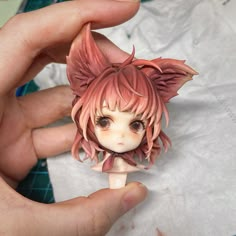 a hand holding a small doll with pink hair on it's head and ears