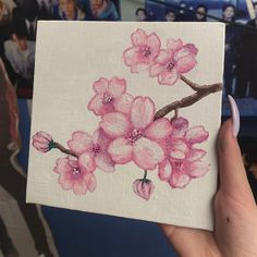 a person holding up a piece of art with pink flowers on it