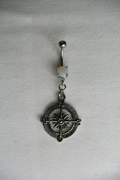 a silver belly ring with a compass and opal bead around the center, on a white background