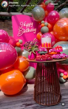 a table topped with cake and balloons on top of a wooden floor next to a pink sign