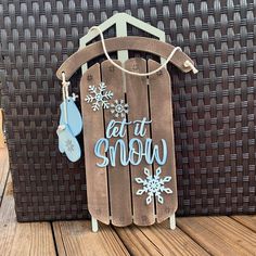 a wooden sign that says let it snow hanging from a clothes hanger on a deck