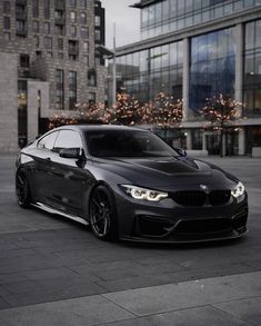 a black car parked in front of a tall building with lights on it's windows