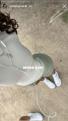 a woman sitting on the ground listening to music with headphones in her ears and wearing white shoes