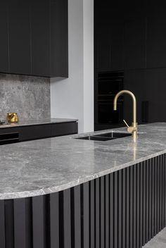 a kitchen with black cabinets and gold faucet on the countertop, along with a marble sink