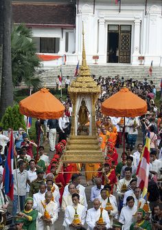 a large group of people standing in front of a building with flags and umbrellas