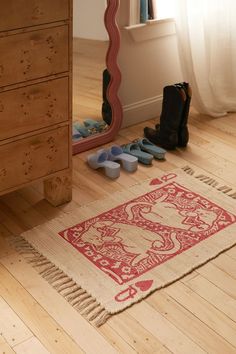 there is a red and white rug on the floor in front of a dresser with shoes next to it