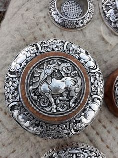 four silver and wood plates with designs on them sitting on a stone surface next to a bottle opener