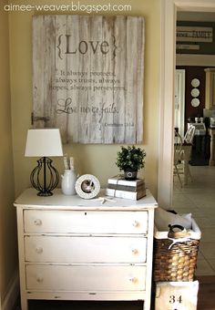 a white dresser sitting in a living room next to a wall hanging on the wall