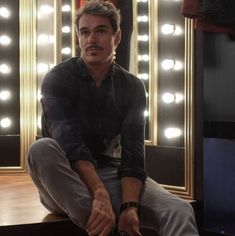 a man sitting on top of a wooden table in front of a mirror with lights