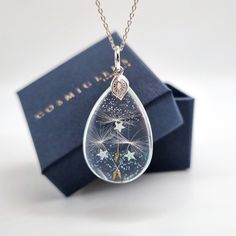 a necklace with a dandelion in the shape of a tear hanging from a box