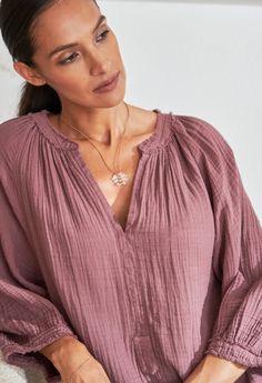 a woman sitting on a couch looking down at her cell phone while wearing a necklace