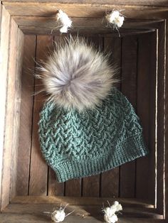 a knitted hat with a fur pom in the middle on top of a wooden box