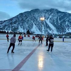 several people playing ice hockey on an outdoor rink with mountains in the background at dusk