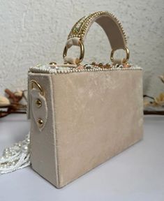 Introducing the Danika Flap Bag, a stunning fusion of bridal elegance and Indian craftsmanship. Hand-beaded with luxurious velvet in enchanting hues of mint, white, and peach, with a beautiful pearl motif, this bag embodies opulence and tradition. Its intricate design, coupled with delicate white suede accents, makes it a standout accessory for brides and lovers of Indian fashion alike. Whether for a wedding ceremony or a cultural celebration, the Danika Flap Bag adds a touch of regal charm to a Luxury Beige Square Clutch, Luxury Rectangular Box Bag With Pearl Handle, Luxury Cream Shoulder Bag For Party, Chic Hand-embellished Rectangular Bag, Chic Hand Embellished Rectangular Bag, Luxury Bag With Pearl Embroidery For Reception, Cream Rectangular Box Bag For Evening, Embellished Rectangular Shoulder Bag For Receptions, Embellished Rectangular Shoulder Bag For Reception