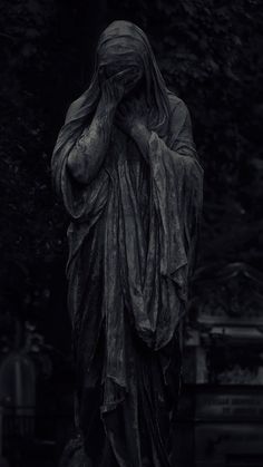 black and white photograph of a statue in front of a tree with its hands on her face